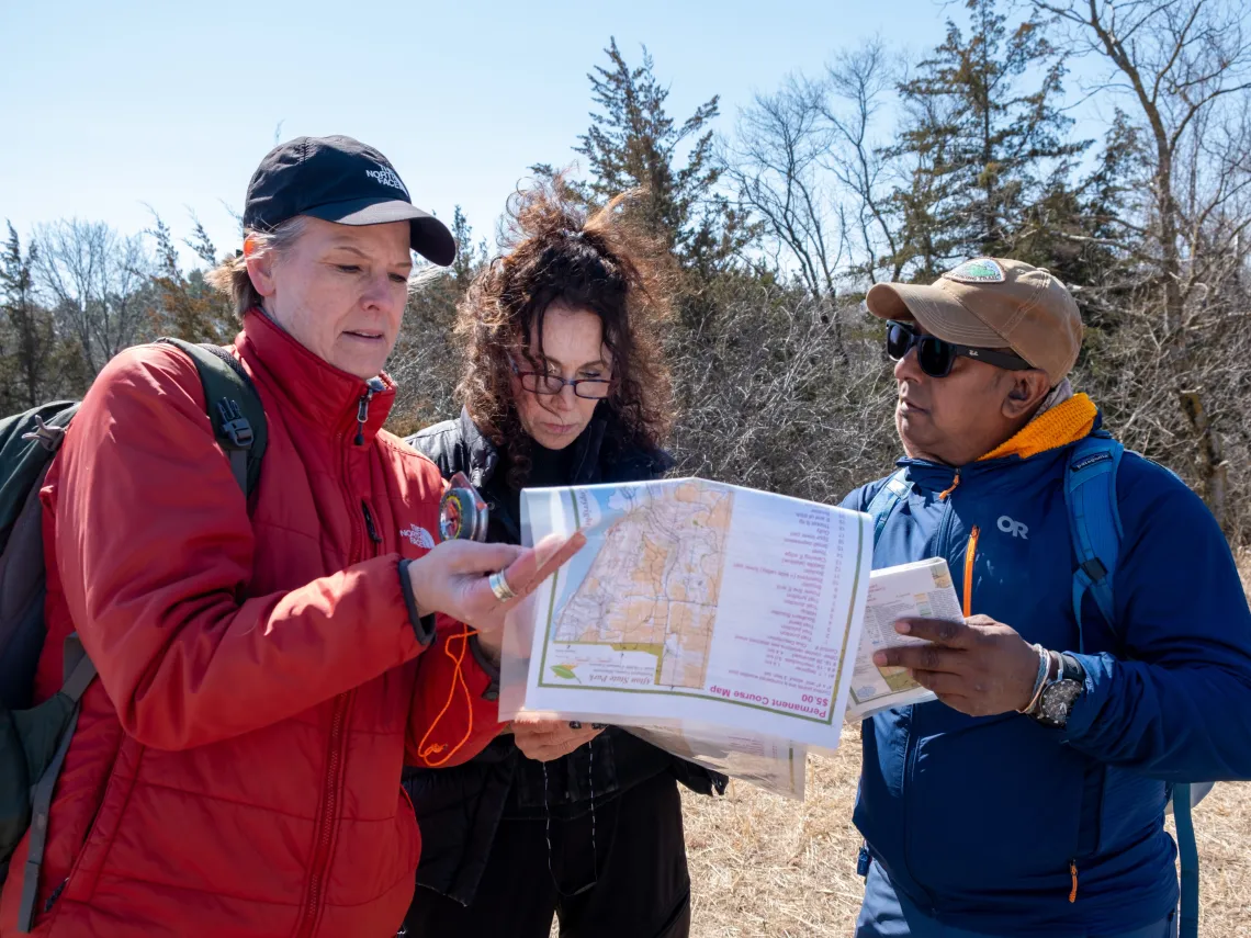 3 hikers consult a map and compass. Photo credit: Devon Young Cupery