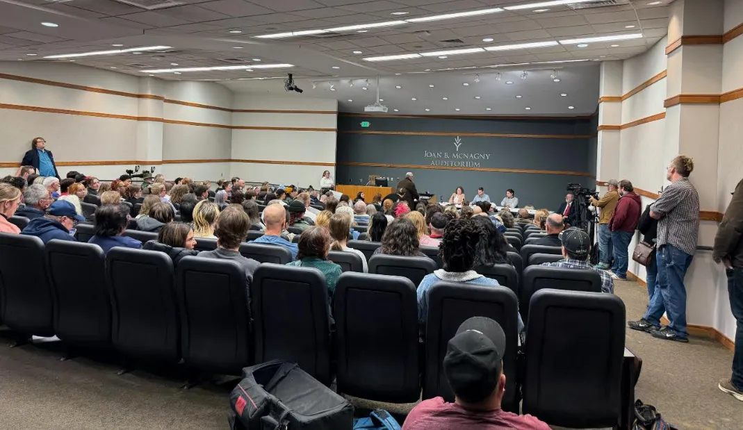 A packed room of folks sitting and standing at a public hearing