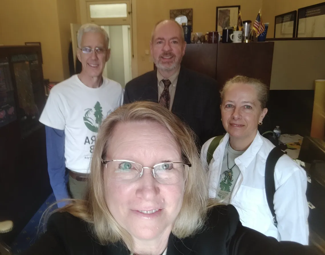 A selfie of a blond haired woman with glasses with three people behind her. They are all smiling.