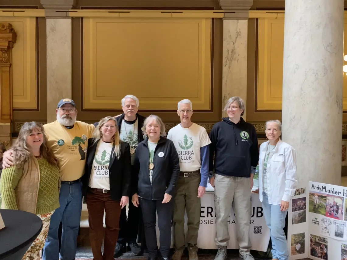A group of eight people indoors at the Statehouse. Some are wearing white t-shirts with the Sierra Club Hoosier Chapter logo. They are smiling for the photo.