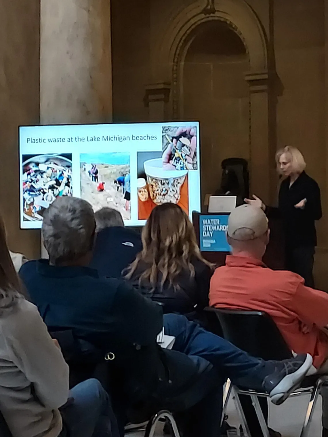 A person giving a presentation on plastic waste at Lake Michigan Beaches. There are people seated listening to them talk. 