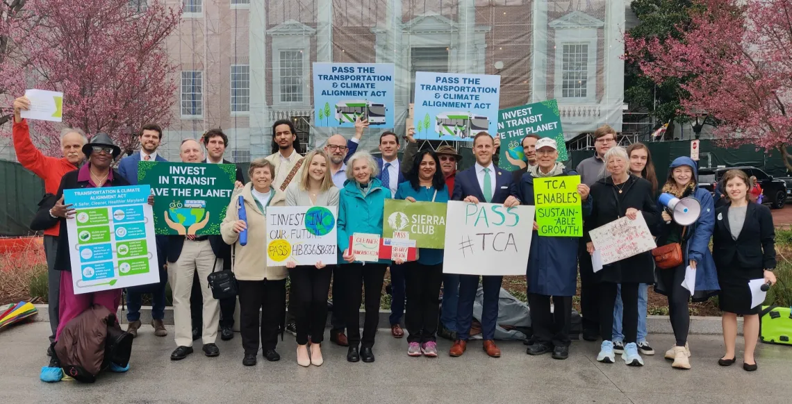 A few dozen people gather with signs supporting transit in front of Maryland capitol with cherry blossoms in the background 