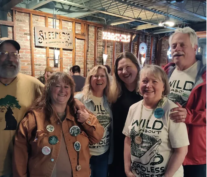 A group of six people indoors at a bar with exposed brick walls. A few of the people are wearing tees that say Wild About Roadless Forests. They are all smiling.