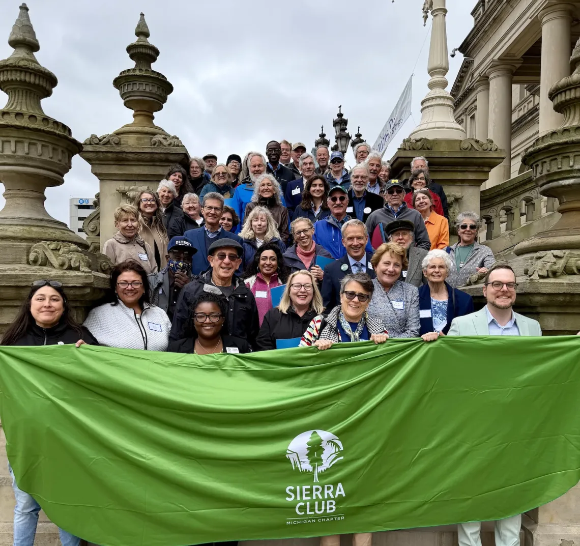 Sierra Club staff and volunteers gather on the steps of the Capitol holding a green Sierra Club banner