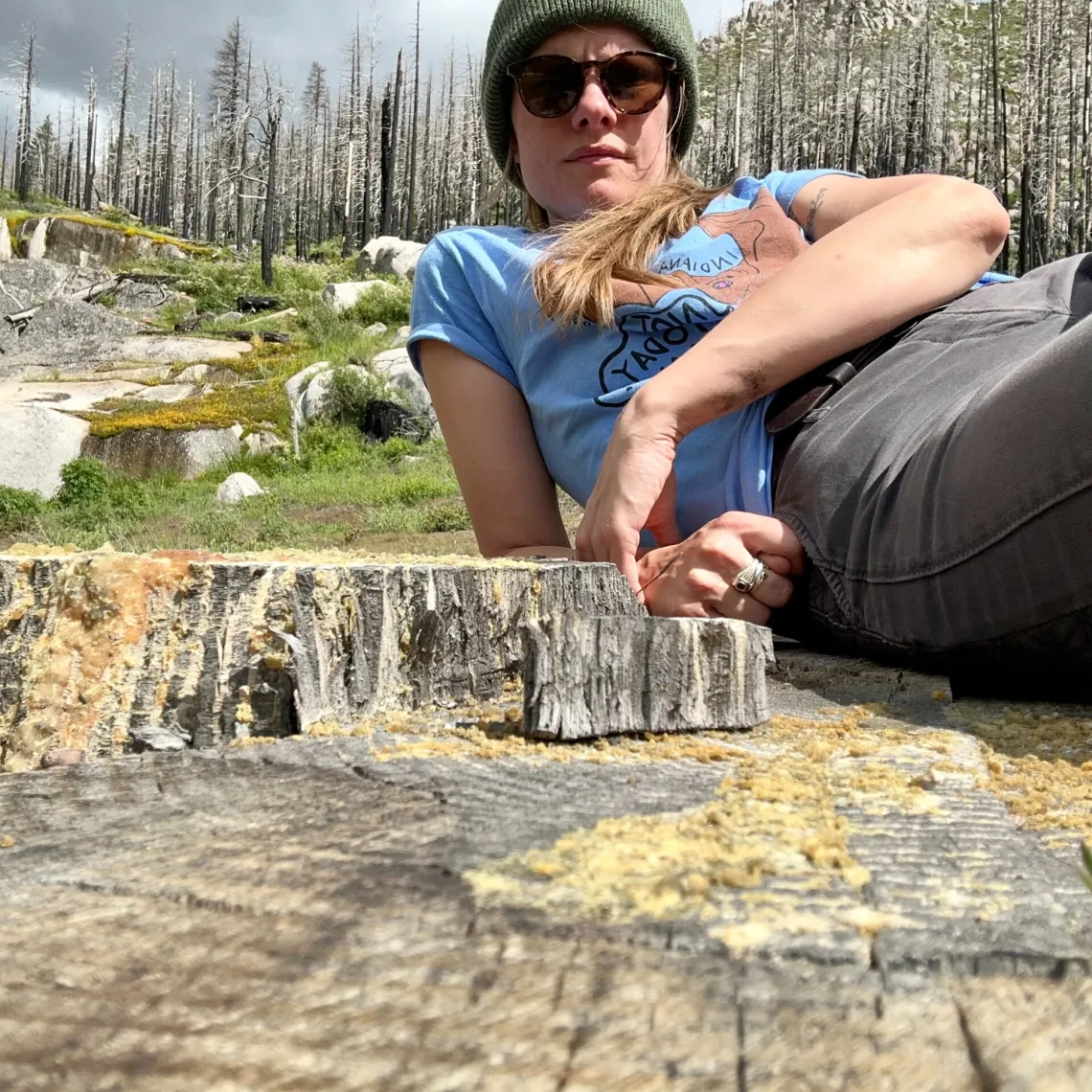 Photo of woman, supine, leaning on elbow with denuded trees in background