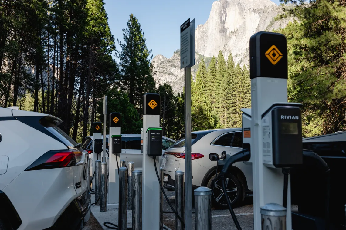 a row of electric vehicle chargers and cars with Yosemite National Park in the background