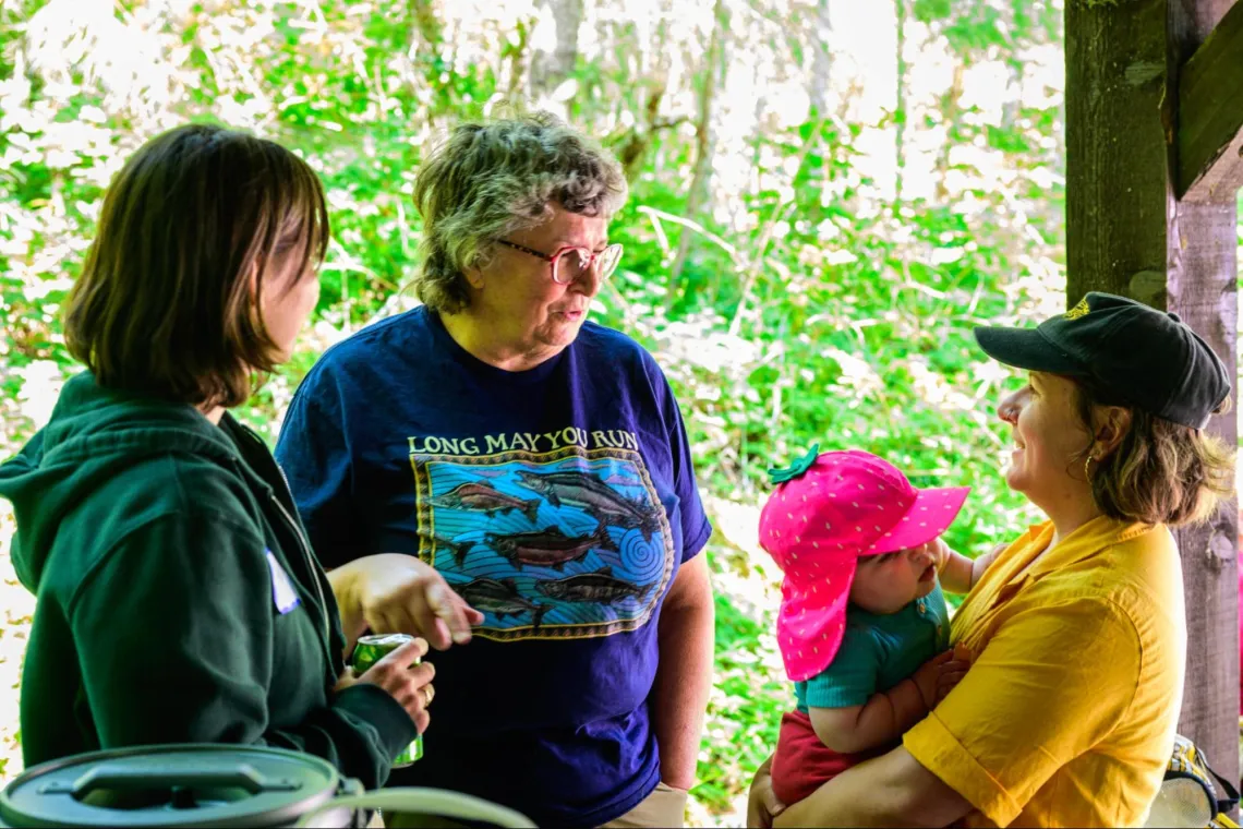 Three women, one holding a baby, speaking in a picnic shelter