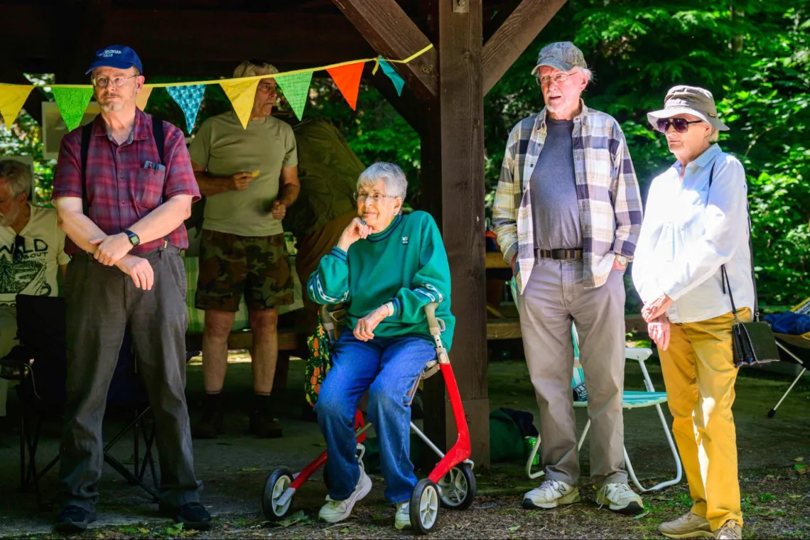 a group of people standing in front of a picnic shelter in a grove of trees