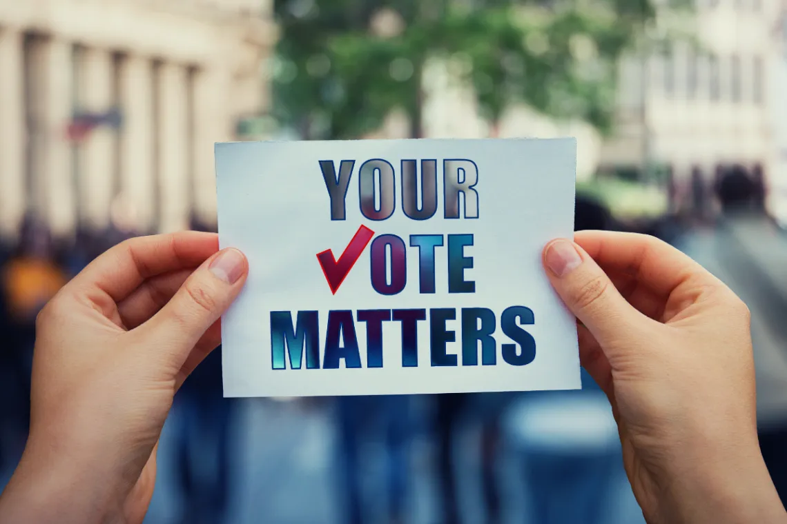 A pair of hands holds up a small sign that reads "Your vote matters"
