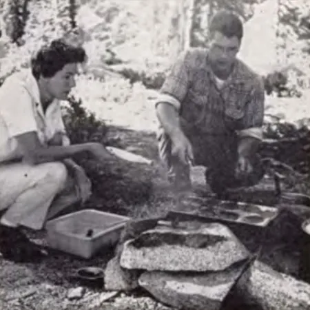 Two people cooking over a campfire