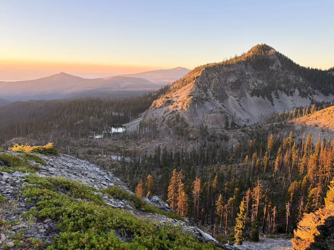 A grand view of mountains, forests, and lakes from on top of a tall mountain.