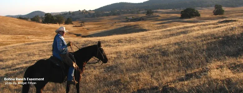 Rancher rides a horse on grassland hills of the Bohna Ranch easement