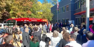 A wide-angle view of people watching Governor Cooper announce his executive order on clean transportation, outside ABB headquarters in Cary, NC. A red electric bus is in the background on this sunny day.