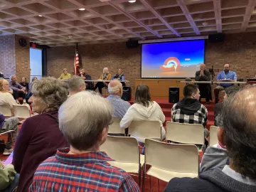 A panel of people in a library. The photo is taken from the audience who are all seated.