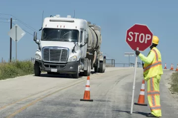 White cement rucks drives down road. A worker with a safety holds a stop sign 