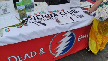 An image of a tabletop at an event. There is a white banner on the table saying Sierra Club Hoosier Chapter, and petitions for folks to sign on the table as well as buttons