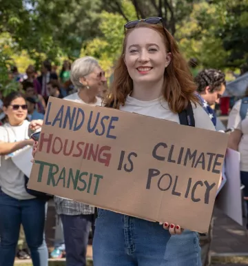 Headshot of Jane Lyons holding a land use transit housing is climate policy sign