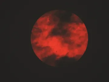 The sun obscured by clouds and filtered by smoke from a wildfire in Canada, photo taken in NYC. The sun is a very strong red color.