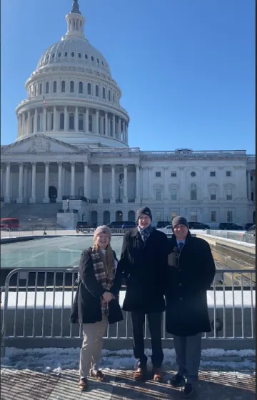 Three people standing outside the Capital building in DC. It's a bright cold day. 