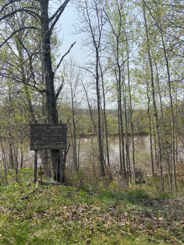 Image of a sign identifying an Ojibwe burial ground in St. Francis Cemetery, with the Nemadji River in the background.