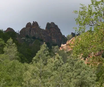 Craggy rocks against gray sky with green brush in front