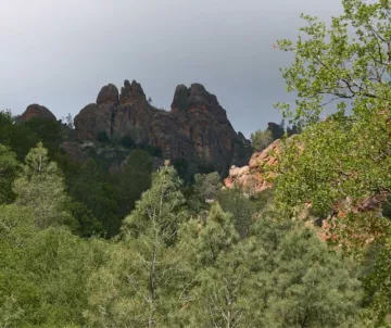 Craggy rocks against gray sky with green brush in front