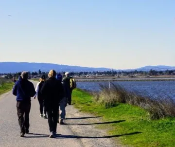Hikers on asphalt path on left, the bay on right, Santa Cruz mountains in background