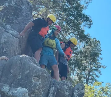A guide and two youth about to jump off of a rock into the river