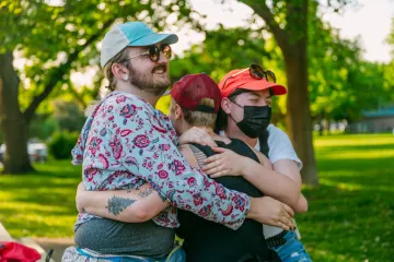 3 people smiling and hugging outdoors