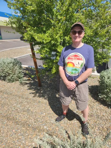 a person in a hat and sunglasses standing next to a tree