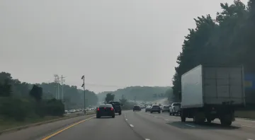Cars moving down a 3 lanes highway in both directions on a day with smoggy skies