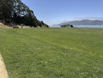 Wide expanse of bermuda grass sports field, water and hills in background