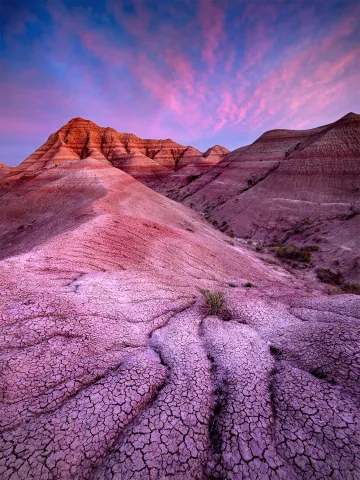 Sunset colors, Cracked earth slope in the foreground leading back to orange striped desert peaks. 