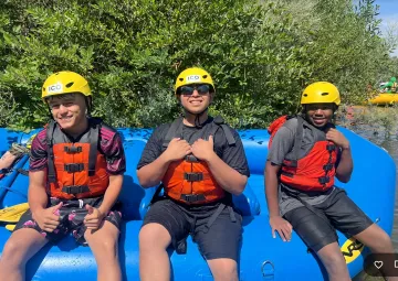 Three male rafters sitting on a blue boat