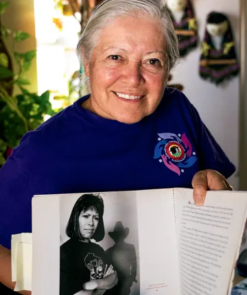 Mily Treviño-Sauceda smiles at the camera and holds up a book with a black-and-white photo of herself as a young organizer.