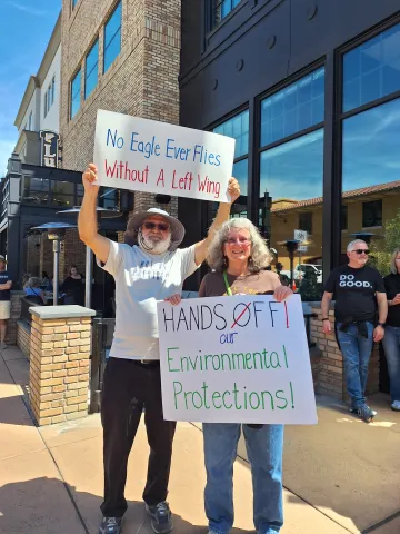 Two people holding signs at the Hands Off Rally in 2025