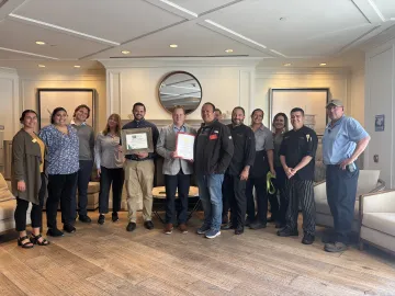 Group of people standing with two holding certificates of Green Business designation
