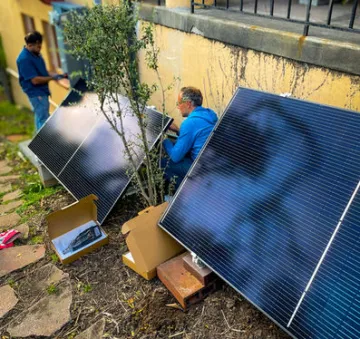 Two men installing plug-in solar panels outside against the walls of a house