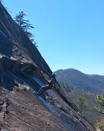 A person rappels down a sloped cliff during a spring 2026 outing in NC led by Lindsey Hildebrand