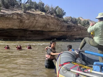 A girl holding a raft in place with other teenagers floating in the water 