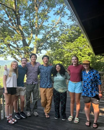 Participants in Sierra Club's SPROG gathering pose on a deck with trees and mountains behind them