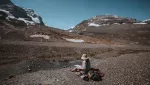 person sitting on ground facing scenic mountain landscape 