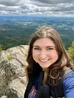 Selfie of Krystal on a rock ledge with green forest and fields below