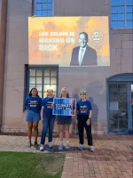 a group wearing blue shirts protests against Lee Zeldin