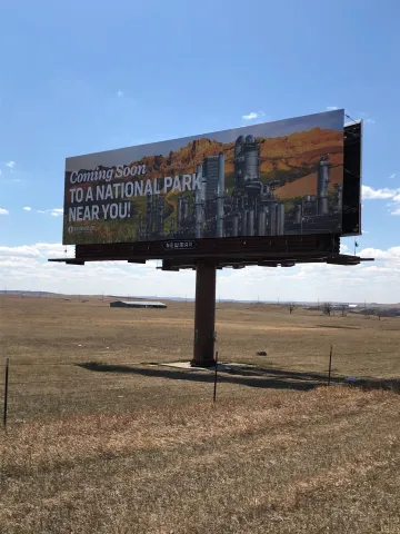 Photo of billboard which has an image of a national park with a refinery in it.