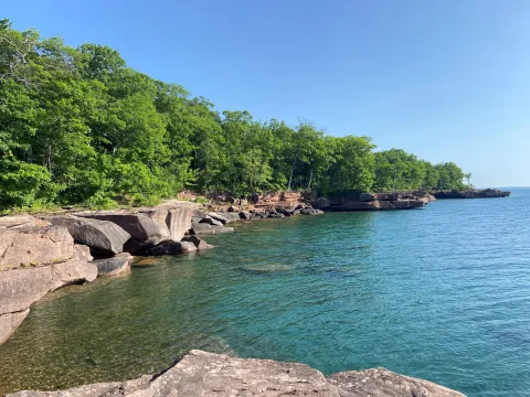 The Lake Superior shoreline from Madeline Island shows blue water and a rocky, tree-covered shore.