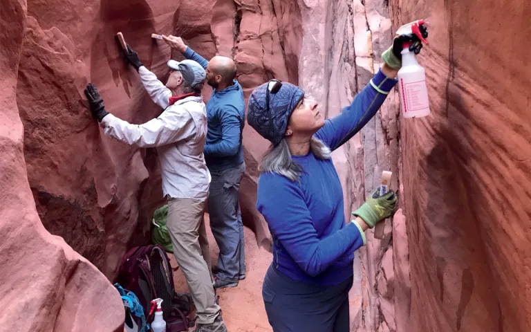 A woman and two men use spray bottles and brushes to clean the walls of the redrock, narrow Spooky Gulch in Grand Staircase–Escalante National Monument.