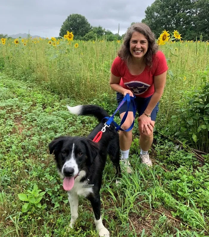 Mayor Kincannon, a white woman with brown hair, poses with her dog in a field of sunflowers.