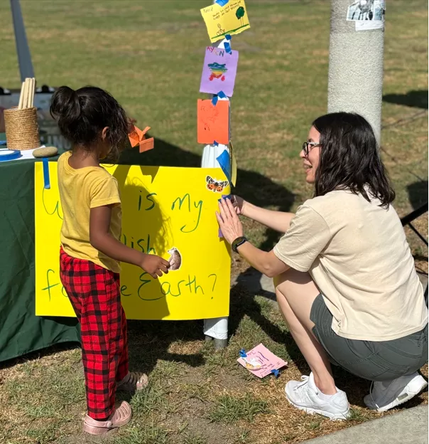 Woman squatting down, talking with a small child in front of a hand-made poster
