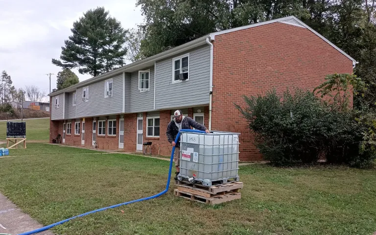 A water tank on a lawn in front a house, with a hose running out of the tank